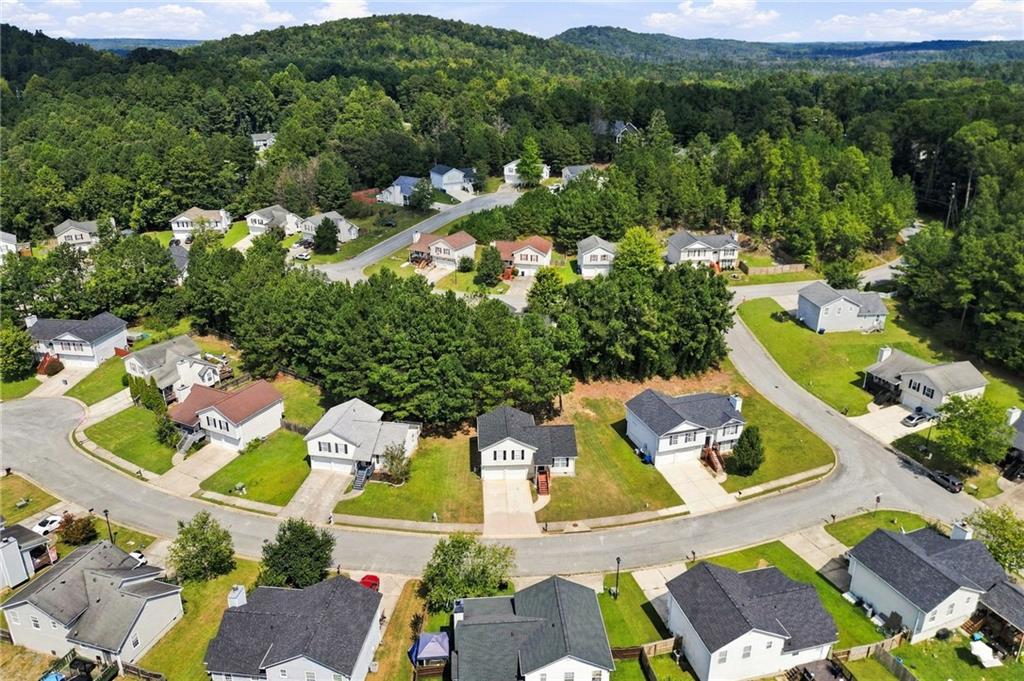 Aerial view of homes along a curving street, with wooded hills beyond.