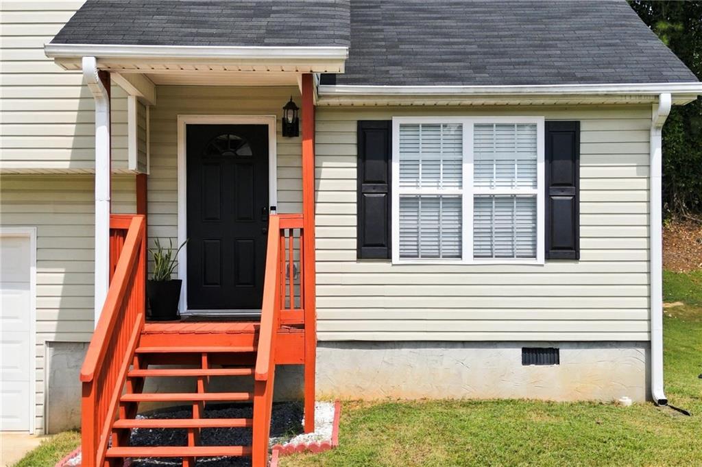 House entrance with bright red-orange porch stairs and railings beside a shuttered window.