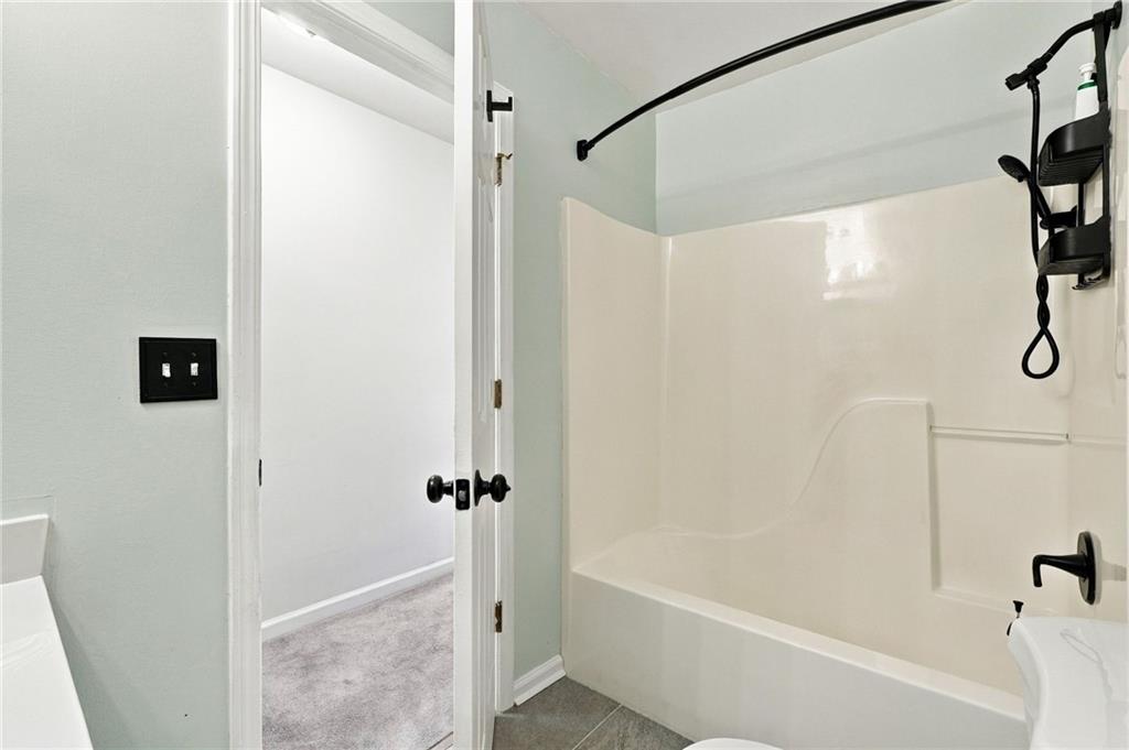 Bathroom with a white tub and shower, black fixtures, and an open door to a carpeted room.
