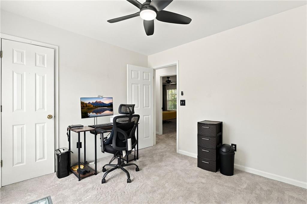 Home office with a desk, black mesh chair, and open doorway to an adjoining room.