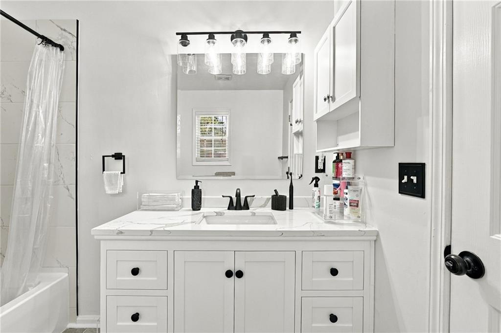 Bathroom with a white double-sink vanity, marble-look counter, large mirror, and tiled bathtub surround.