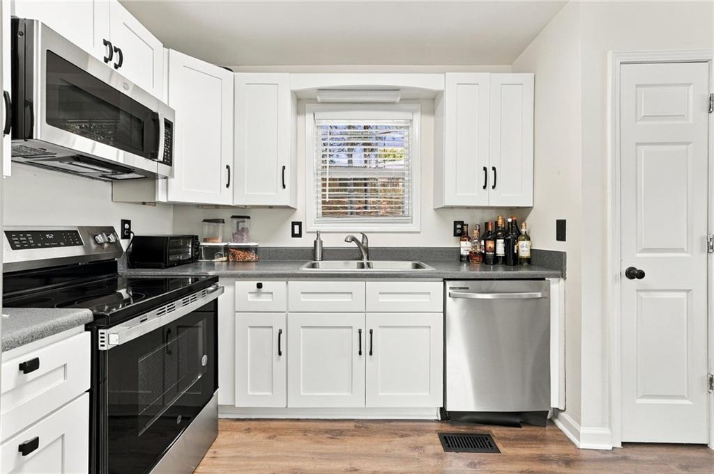 Kitchen with white shaker cabinets, gray countertops, stainless dishwasher, and a window above the sink.