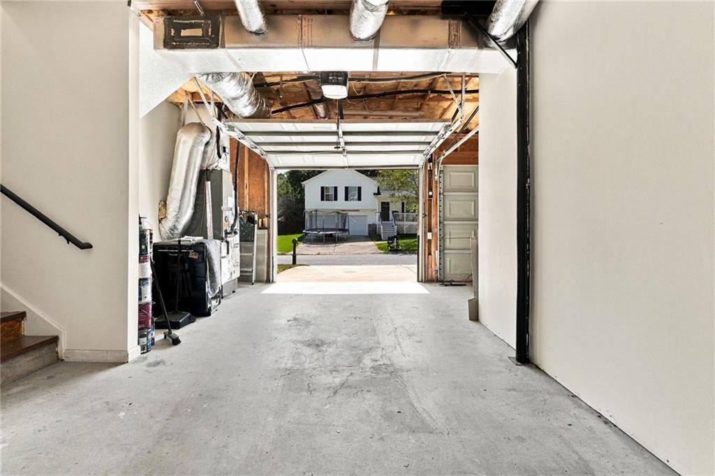 Garage with an open overhead door, exposed ceiling ducts, and a view toward a neighboring house.