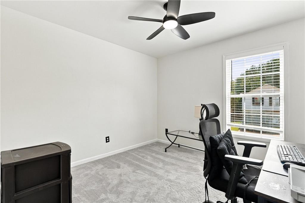 Home office with gray carpet, a black desk chair, computer desk, and window with blinds.