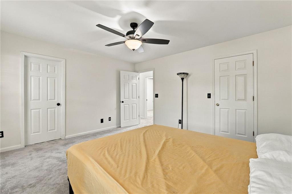 Bedroom with a mustard-colored bedspread, gray carpet, and ceiling fan.