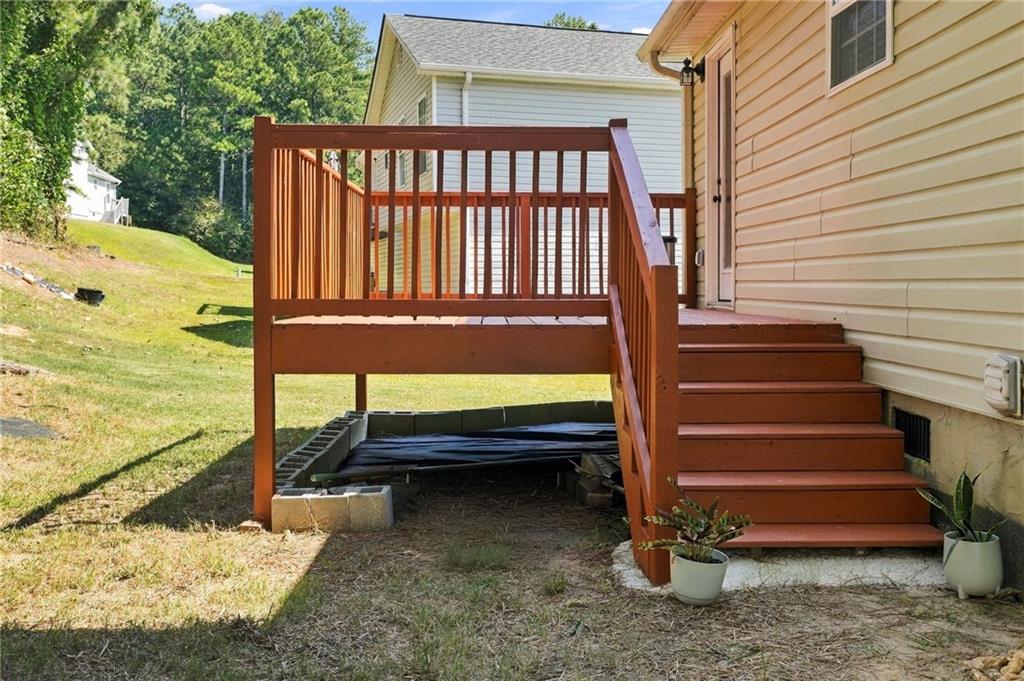 Raised wooden deck and stairs beside a beige-sided home, with potted plants and a grassy yard.
