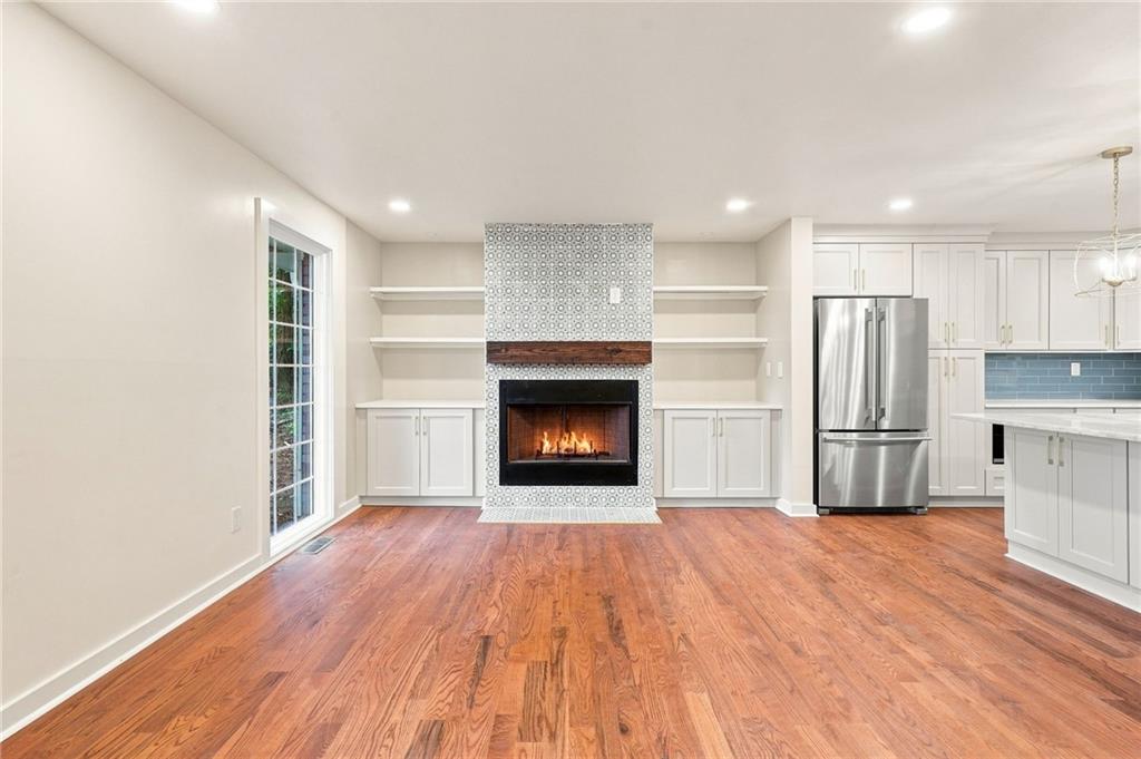 Open-plan living area and kitchen with a tiled fireplace, stainless steel refrigerator, and hardwood floors.