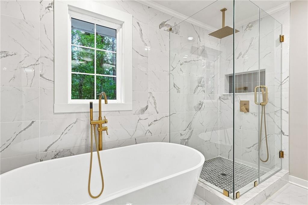 Bathroom with a freestanding soaking tub, glass shower, marble-look tile, and gold fixtures.