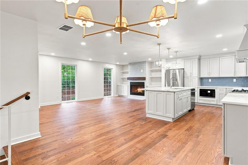 Open kitchen and living area with hardwood floors, a white island, and a fireplace.