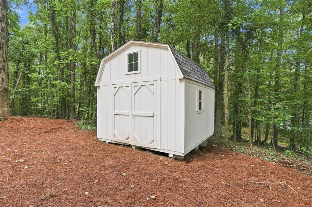 White storage shed with double doors and small windows, surrounded by trees.