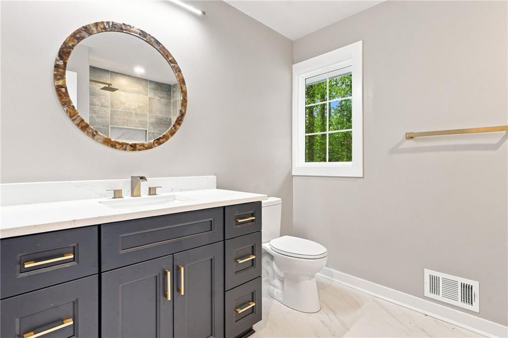 Bathroom with a dark vanity, round mirror, and window overlooking greenery.