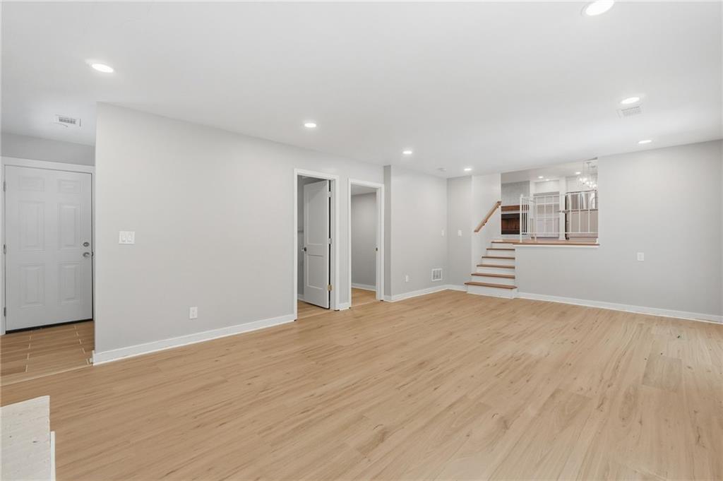 Vacant living area with light wood flooring and stairs leading to an open kitchen.