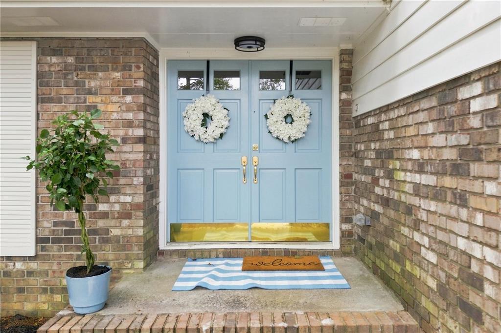 Covered brick entry with pale blue double doors, white wreaths, and a potted plant.