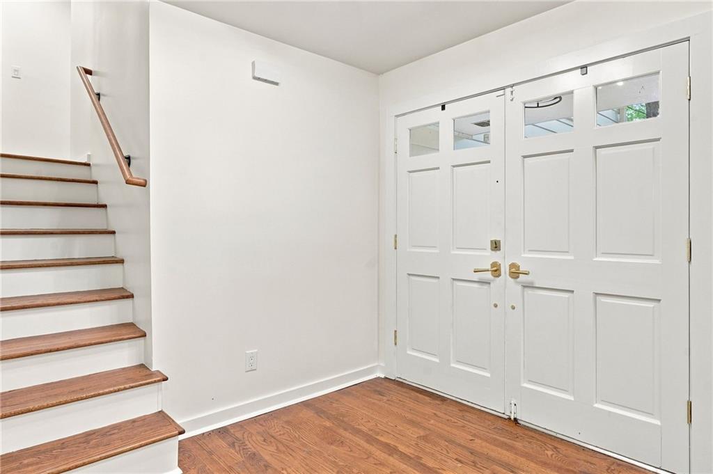 Entryway with white double doors, wood flooring, and a staircase with wood treads.