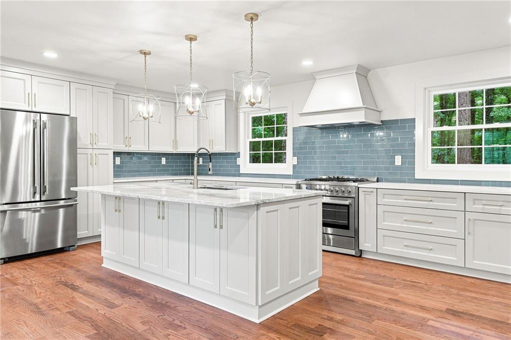 Kitchen with a large white island, blue-gray tile backsplash, and stainless steel appliances.
