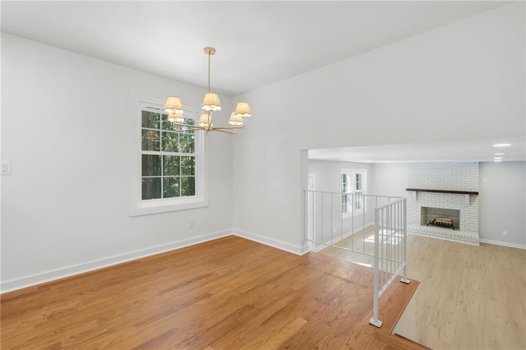 Empty dining room with hardwood floors and chandelier, opening to a living area with a white brick fireplace.