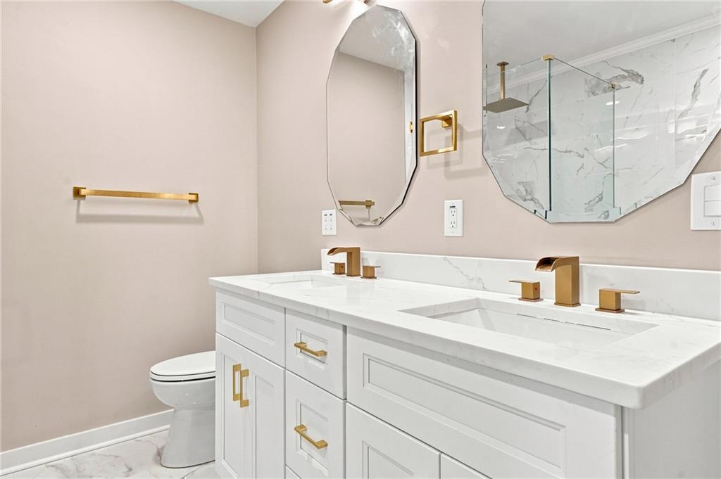 Bathroom with a white double vanity, marble-look counters, gold fixtures, and two angular mirrors.