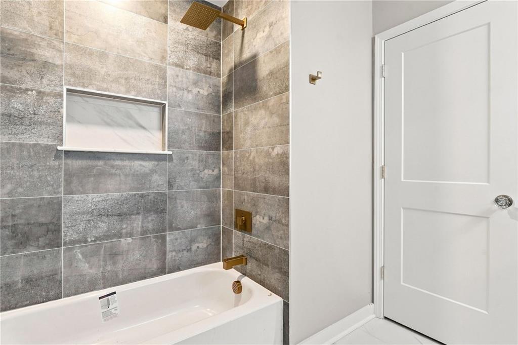 Bathroom tub and tiled shower with gold fixtures and a recessed wall niche.