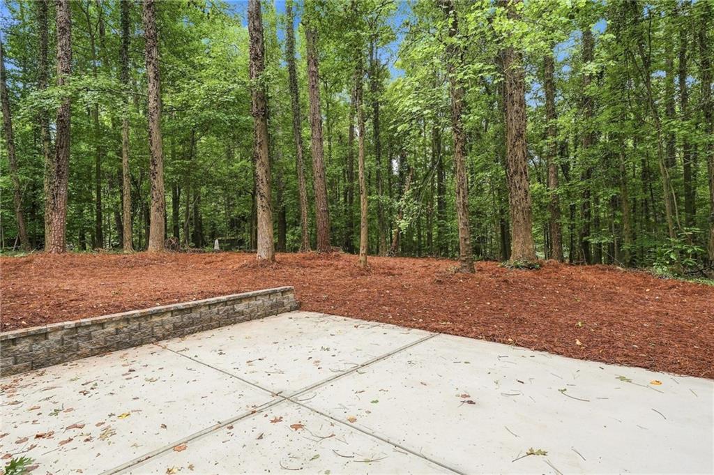 Concrete patio beside a low stone retaining wall, overlooking a wooded yard.
