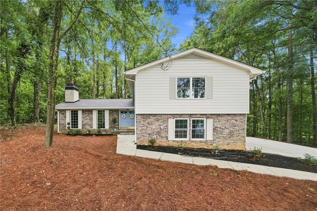 Split-level home with brick and white siding, a blue front door, and a wooded yard.