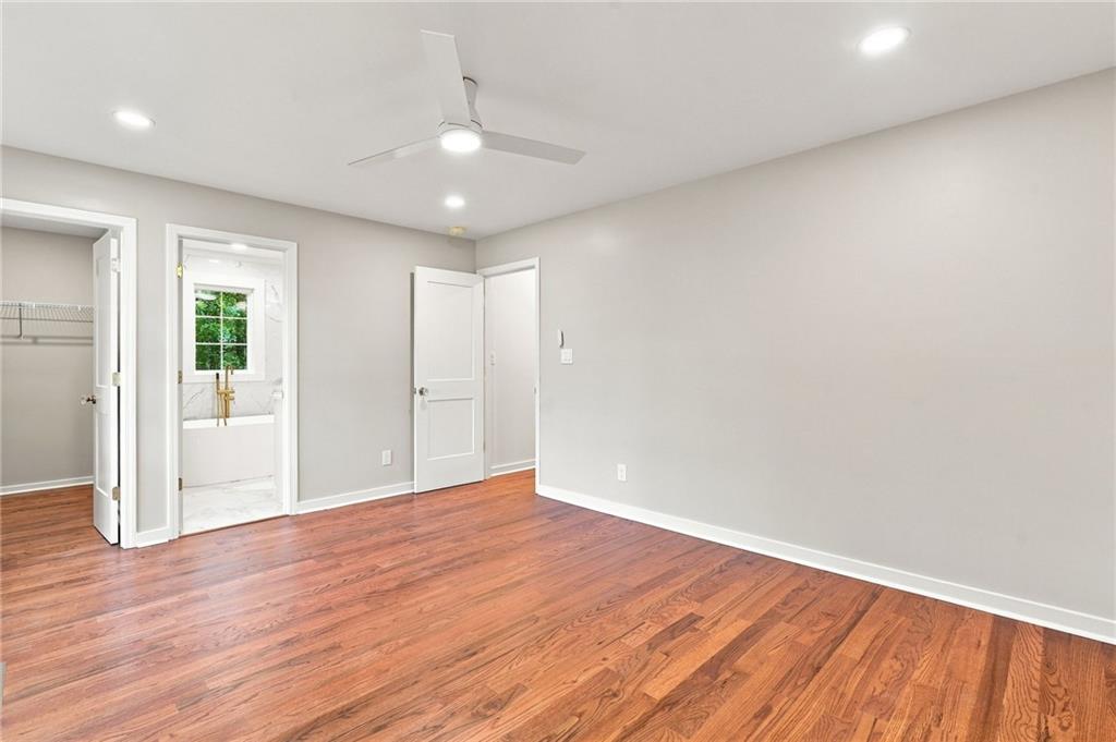 Vacant bedroom with hardwood floors, a ceiling fan, and adjoining closet and bathroom.