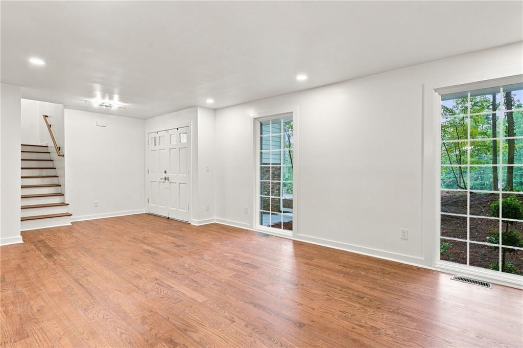 Empty room with hardwood floors, a staircase, and large windows overlooking trees.