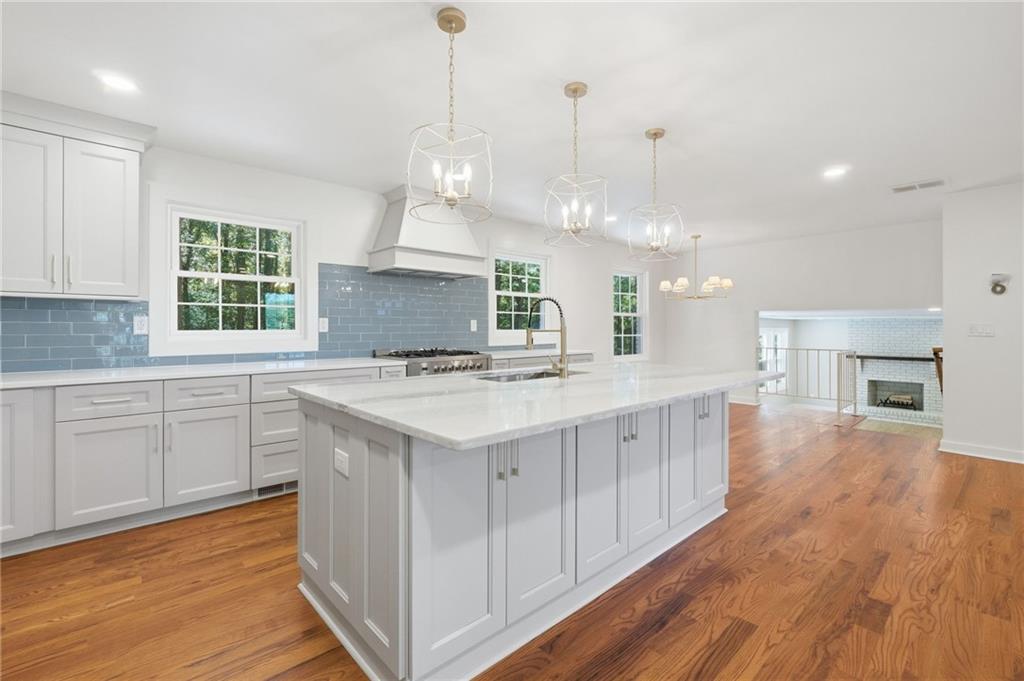 Kitchen with a large white island, blue tile backsplash, and warm hardwood floors.