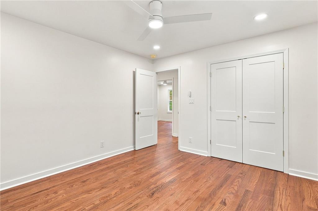 Empty bedroom with reddish hardwood floors, a ceiling fan, and double closet doors.