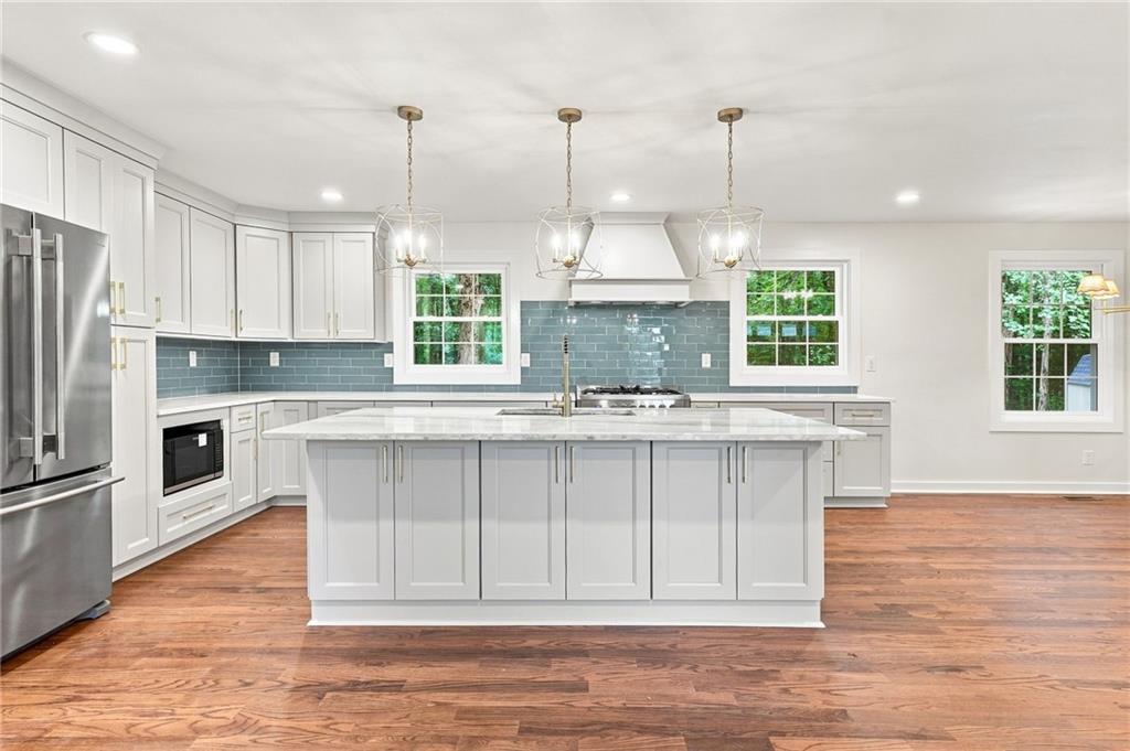 Bright kitchen with a large white island, blue-green tile backsplash, and wood floors.