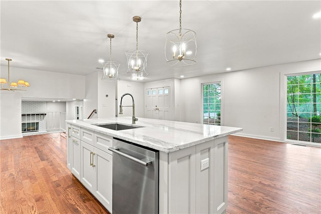 Open kitchen with a large white island, stone countertop, and hardwood floors extending to a fireplace.