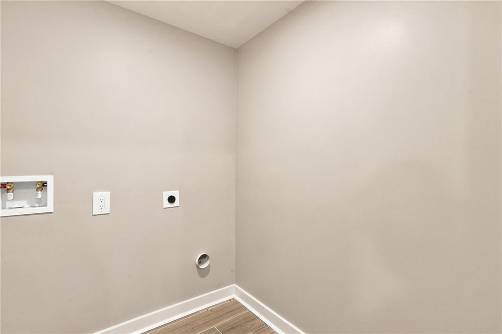 Empty laundry area with washer hookups, outlets, and wood-look flooring.