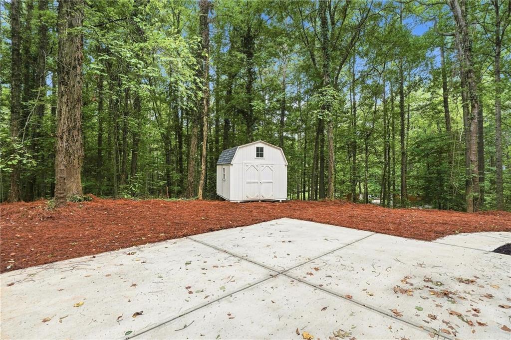 White storage shed beside a concrete driveway, surrounded by mature trees.