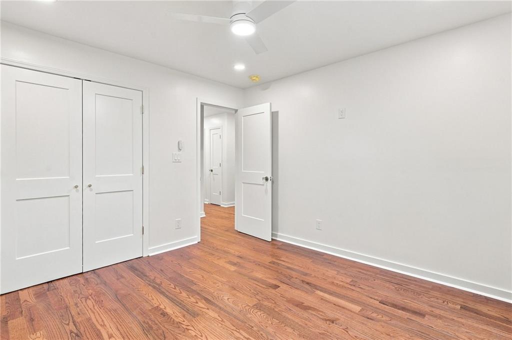 Empty bedroom with white closet doors, an open doorway, and hardwood floors.