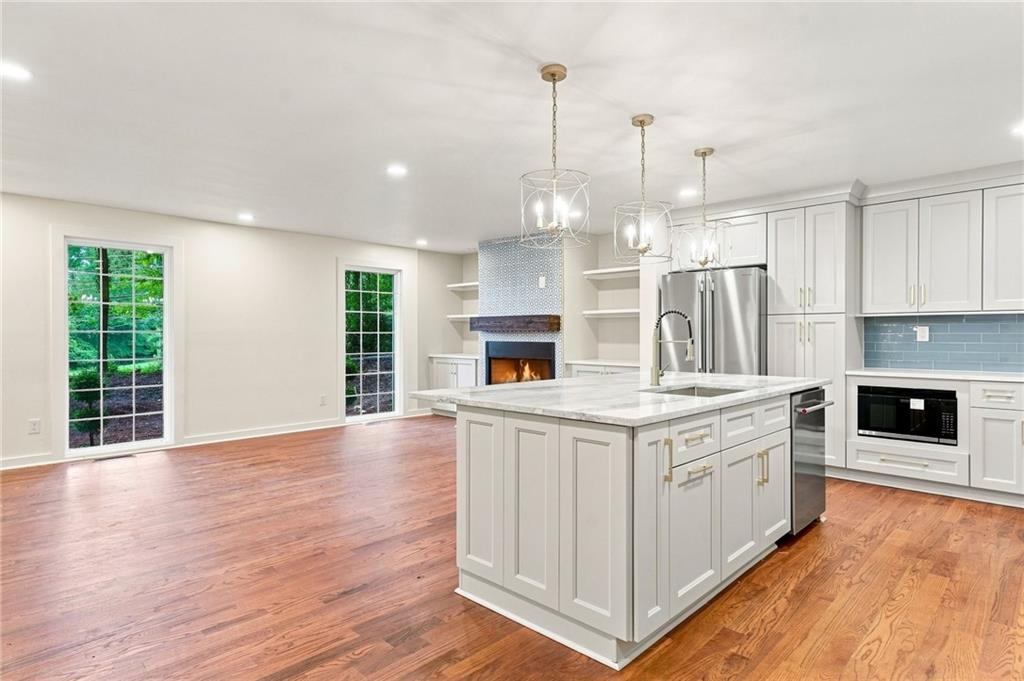 Renovated kitchen with a large white island, stainless steel appliances, hardwood floors, and a fireplace.