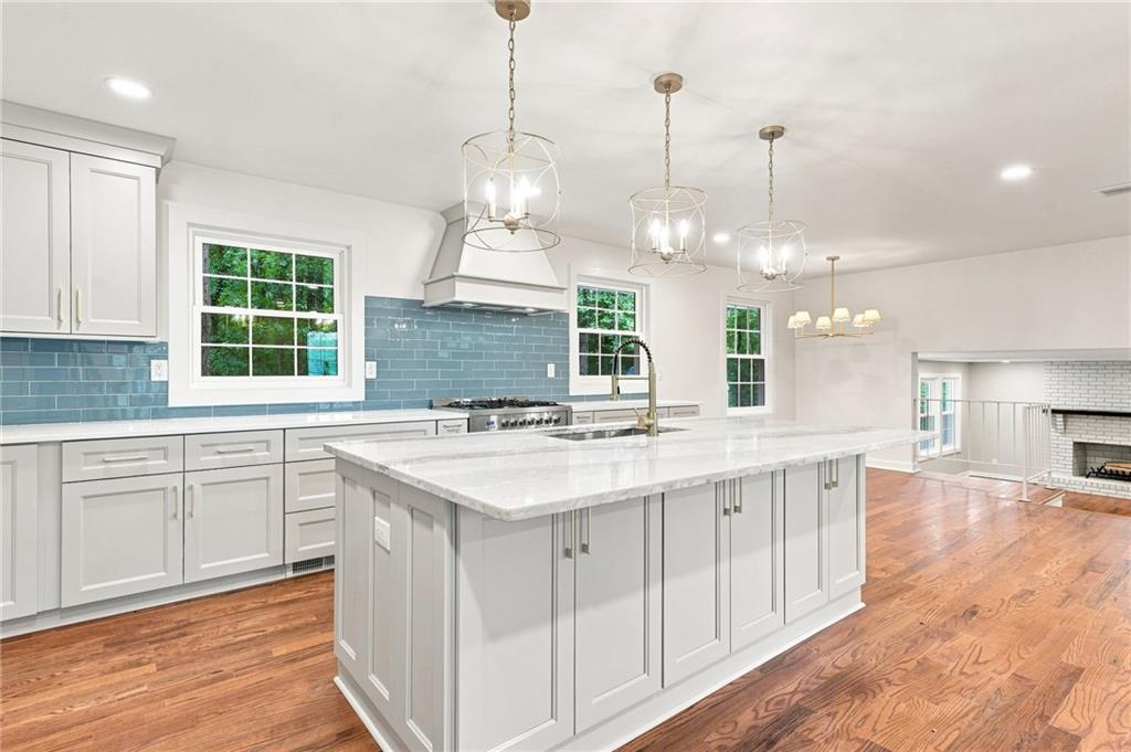 Bright kitchen with a large marble island, blue tile backsplash, and hardwood floors.
