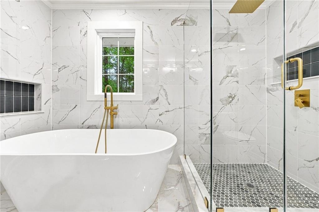 Bathroom with a freestanding soaking tub, marble-look tile, and glass shower with dark hexagonal floor.