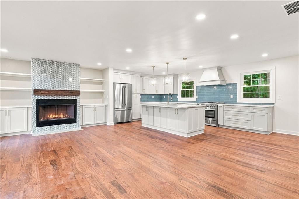 Open kitchen with white cabinets, blue tile backsplash, hardwood floors, and a tiled fireplace.