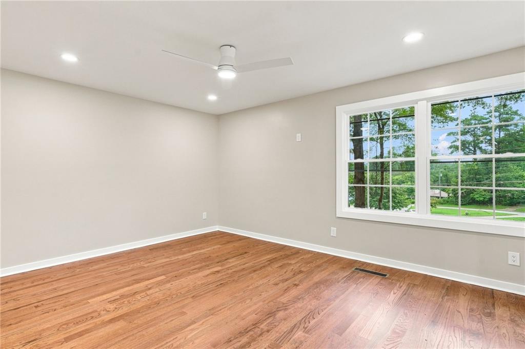 Empty room with hardwood floors, a ceiling fan, and a large window overlooking trees.