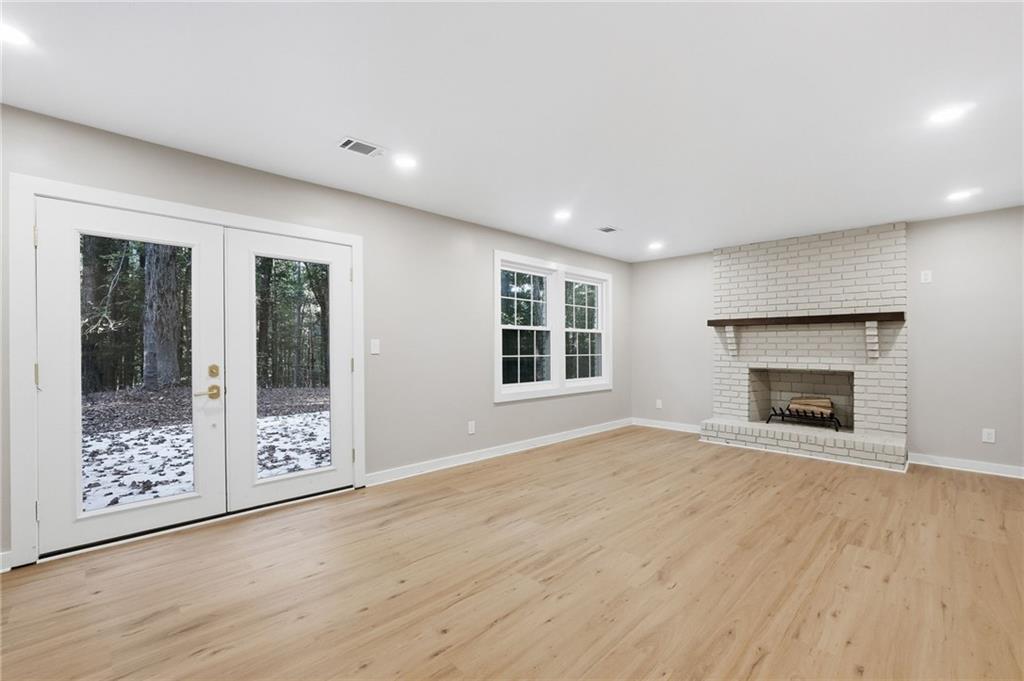 Empty living room with a white brick fireplace and glass doors overlooking a snowy wooded yard.