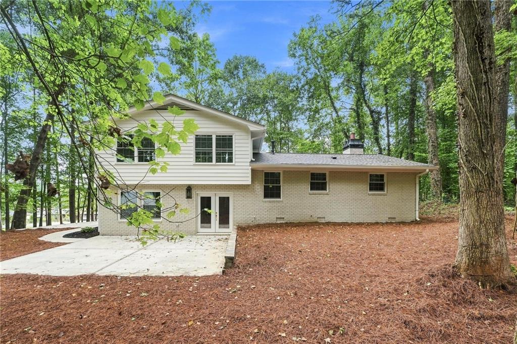 Two-story house with light siding and brick, a concrete driveway, and mature trees.