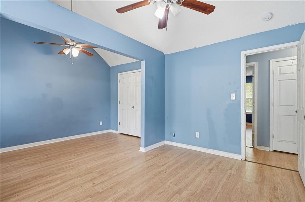 Empty bedroom with blue walls, light wood flooring, and two ceiling fans.