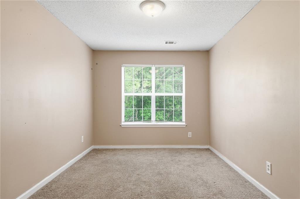 Empty carpeted room with beige walls and a wide window overlooking greenery.