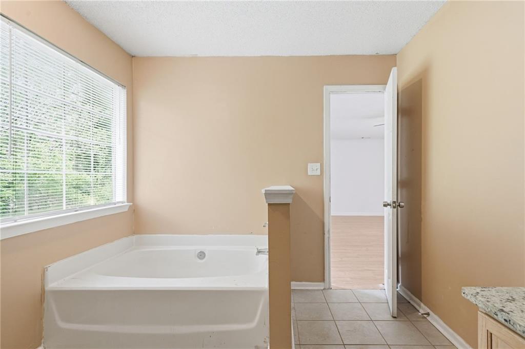 Bathroom with a large soaking tub beneath a wide window and an open doorway to an adjoining room.