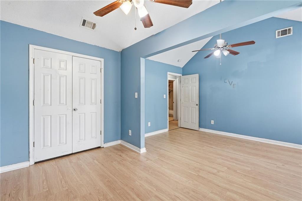 Empty blue-walled room with light wood floors, white closet doors, and two ceiling fans.