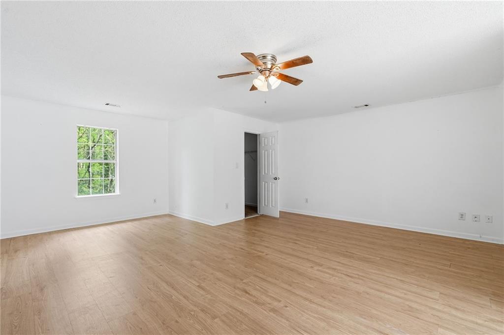 Empty room with light wood floors, a ceiling fan, and a window overlooking greenery.