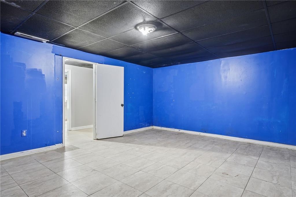 Empty room with bright blue walls, large gray floor tiles, and a dark drop ceiling.