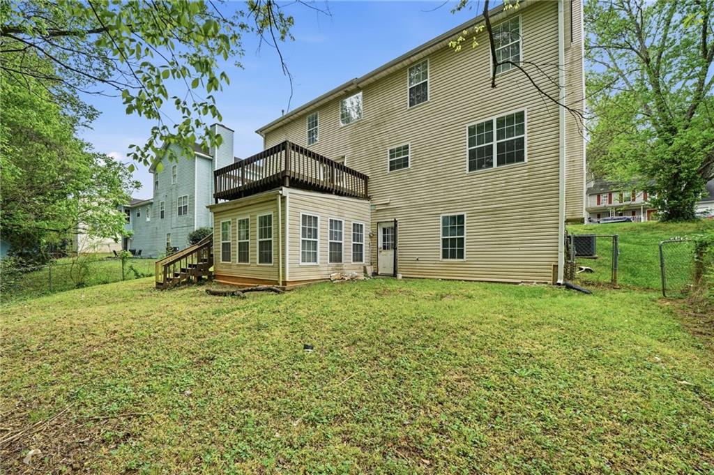 Rear of a two-story beige house with a raised deck overlooking a grassy, tree-lined yard.