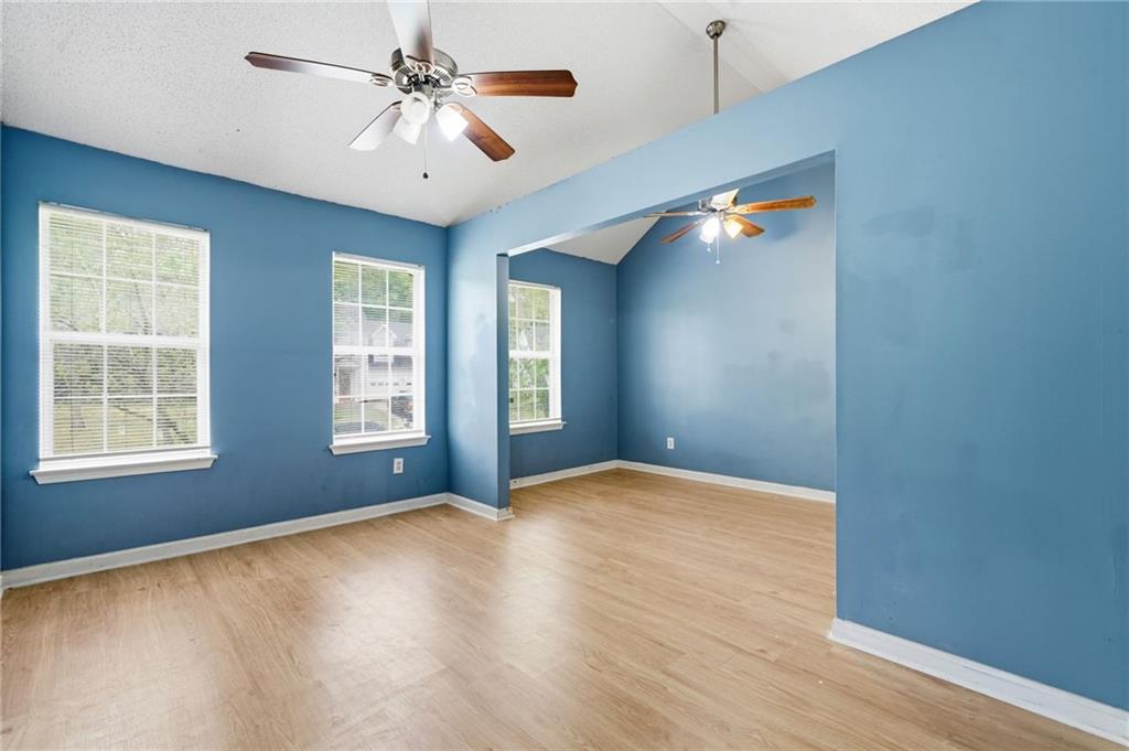 Empty blue-walled room with light wood floors, two windows, and ceiling fans.