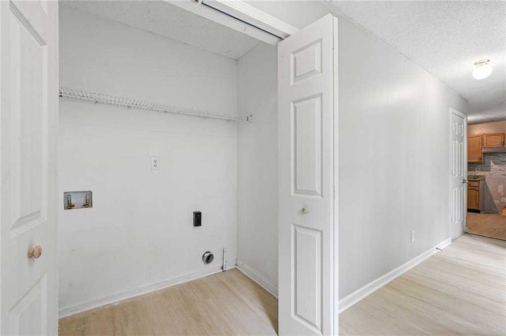 Empty laundry closet with wire shelf and washer hookups beside a hallway leading to the kitchen.