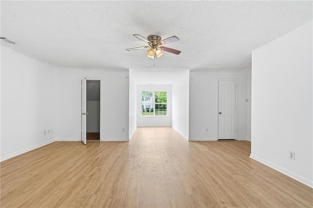 Empty room with light wood floors, a ceiling fan, and a large window.
